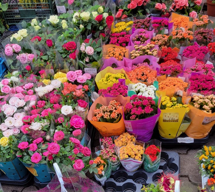 A vibrant display of floral arrangements at a flower market, featuring a variety of fresh flowers in shades of pink, white, yellow, orange, and red. The arrangements include roses, carnations, and oth